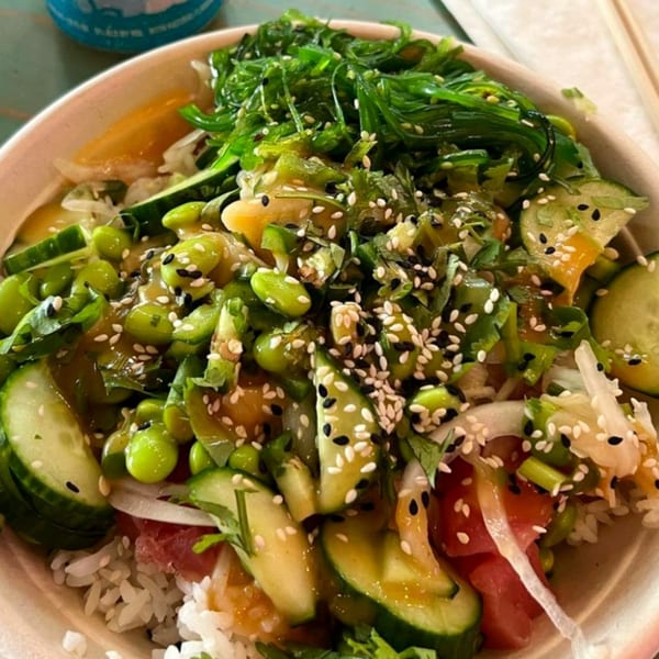 Close-up of a Hawaiian poke bowl with rice, tuna, seaweed, edamame, cucumbers, and sesame seeds.