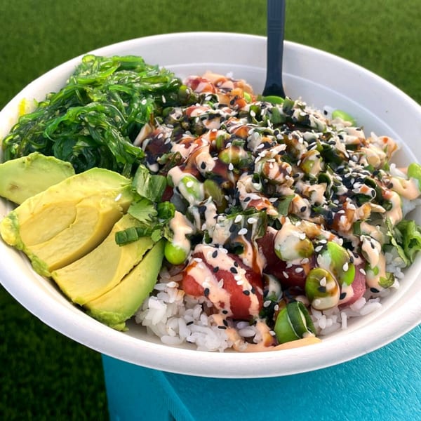 A Hawaiian poke bowl with rice, tuna, avocado, seaweed, and sauces, on a blue surface.