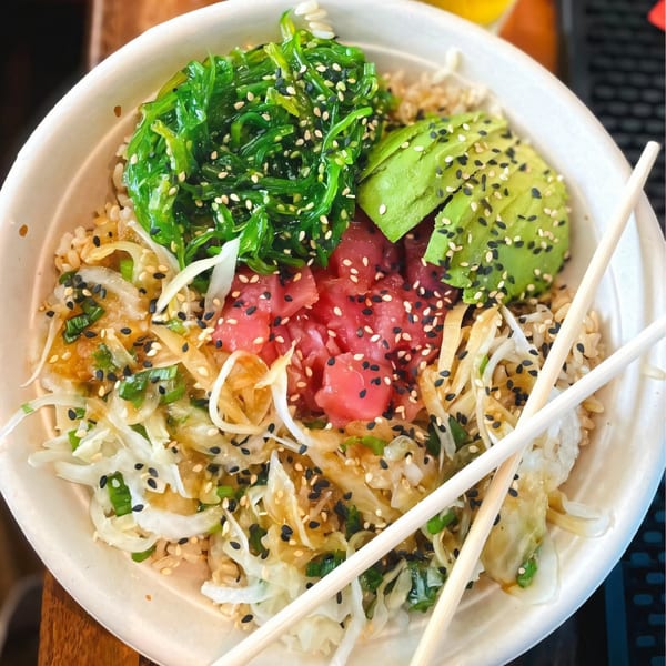 A vibrant Hawaiian poke bowl with tuna, avocado, seaweed, and rice, garnished with sesame seeds.