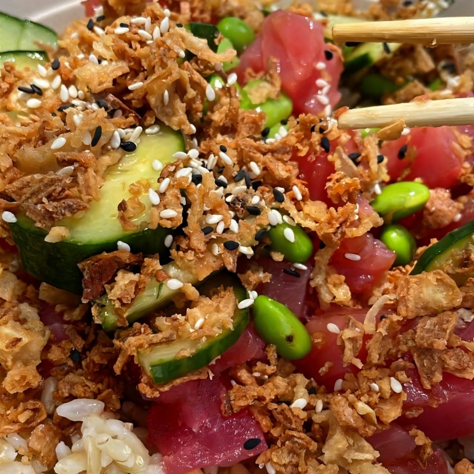 Close-up of a Hawaiian poke bowl with tuna, cucumbers, edamame, crispy onions, and sesame seeds.
