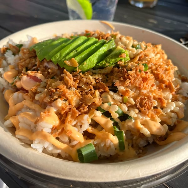 A Hawaiian poke bowl with rice, avocado, crispy onions, and a creamy orange sauce.