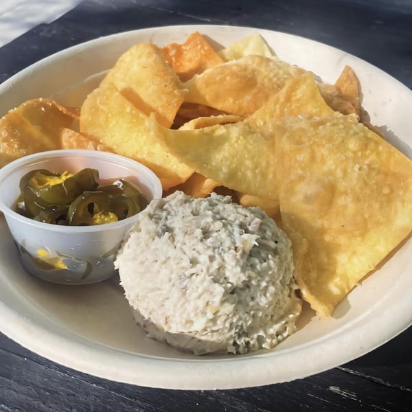A white bowl filled with crispy wonton chips, a scoop of tuna dip, and a side of pickled jalapeños.